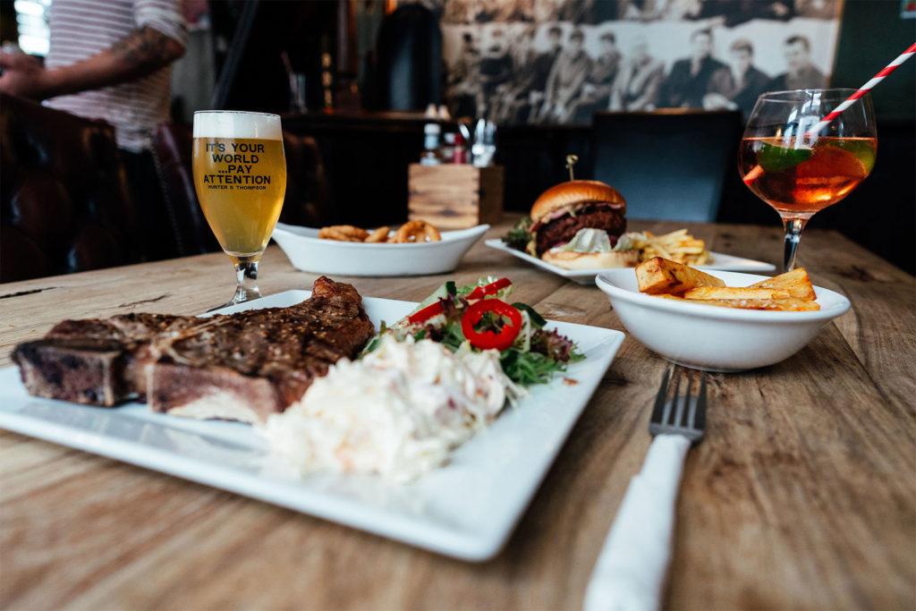 A table laid with steak, a burger, onion rings and drinks in the pub